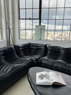 a black leather sectional sofa with an open book on it in front of a large window