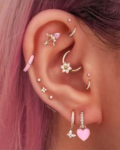 a woman with pink hair wearing three different ear piercings and one has a heart