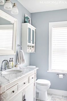 a bathroom with blue walls and white fixtures, including a sink, toilet, and window