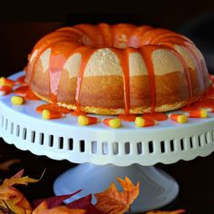 a bundt cake with orange icing sitting on a white plate next to autumn leaves