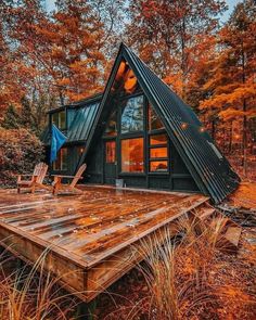 a small cabin in the woods with a deck and chairs on it's side