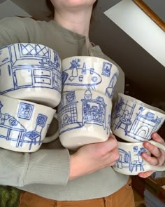 a woman holding four cups with blue drawings on them