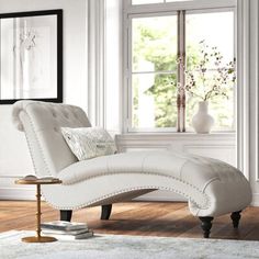 a white chaise lounge chair sitting on top of a hard wood floor next to a window