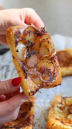 someone holding up a piece of food in front of the camera with french onion tart on it