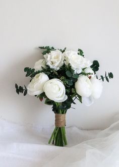 a bouquet of white flowers sitting on top of a white cloth covered tablecloth next to a wall