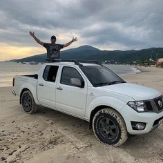 a man standing on top of a white pick up truck in the sand at the beach