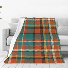 an orange and green plaid blanket sitting on top of a couch next to a plant