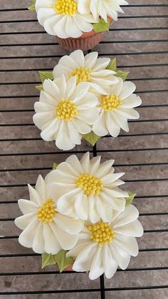 three cupcakes with white and yellow flowers sitting on top of a wire rack