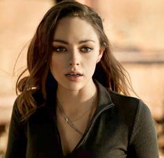 a close up of a person wearing a black shirt and necklace with an evil look on her face