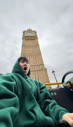 a man in a green hoodie with his mouth open and big ben in the background