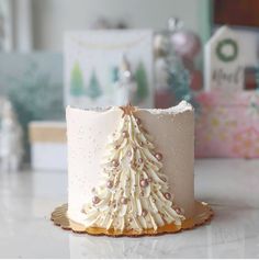 a white frosted cake with a christmas tree decoration on the top and gold trim