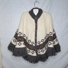 "Darling handknit fringed shawl or cape with metal button front closures. It features a stand up collar and fringed hem. This was handknit and not manufactured. Unclear if the maker used acrylic yarn, wool, or a blend. It is soft and cozy. It does not have pockets or openings. More cape or poncho like, as shown. One size fits most (women large to XL) No set shoulder bust or waist. Length 26\" (side collar to bottom of fringe) Pair it with jeans." Vintage Winter Poncho One Size, One Size Vintage Poncho For Winter, Winter Fringe Cape Outerwear, Vintage One-size Winter Poncho, Wool Cape One Size For Winter, One Size Wool Winter Cape, One-size Wool Winter Cape, One Size Winter Outerwear With Fringe, Winter Shawl Cape With Fringe