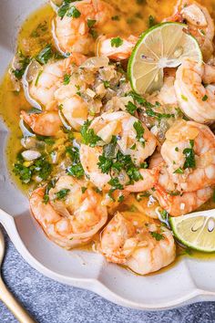 a white bowl filled with shrimp and garnished with cilantro, parsley and lime