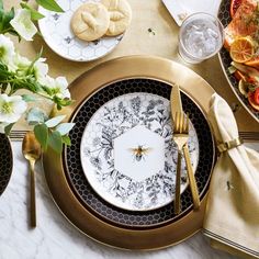 the table is set with plates, silverware and gold utensils on it