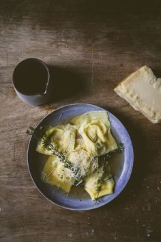 a plate of ravioli with parmesan cheese and herbs next to a cup of coffee