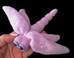 a hand holding a pink stuffed animal with wings