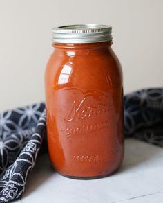 a mason jar filled with tomato sauce sitting on top of a table next to a black and white cloth