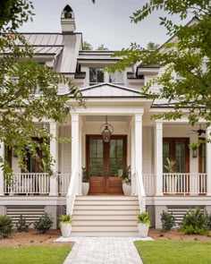 a white house with two story porchs and columns on the front door, surrounded by greenery