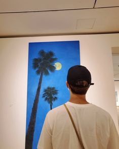 a man standing in front of a painting with palm trees on it and the moon behind him