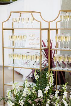 there are many wine glasses on the shelf with flowers in front of it and one is filled with champagne