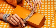 two hands holding an orange gift box on a polka dot tablecloth