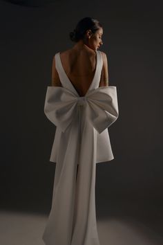 the back of a woman's white dress with a large bow on her shoulder