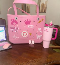 a pink purse sitting on top of a wooden table next to a laptop and cup