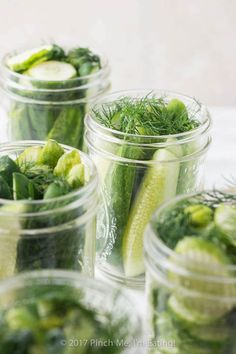 several jars filled with pickles and cucumbers on top of a white table