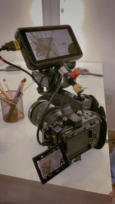 a video camera sitting on top of a table next to a cup with pens and pencils