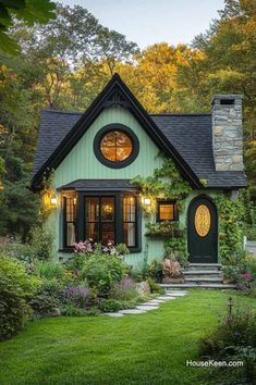 a small green house surrounded by greenery and flowers in the front yard, with a stone walkway leading up to it