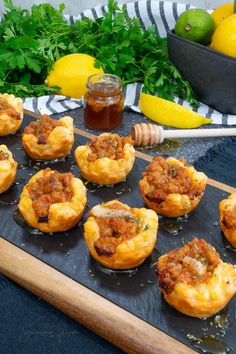 several mini muffins with meat and sauce on a tray next to lemons