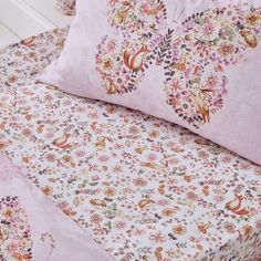 a bed covered in pink sheets and pillows with floral designs on the pillowcases