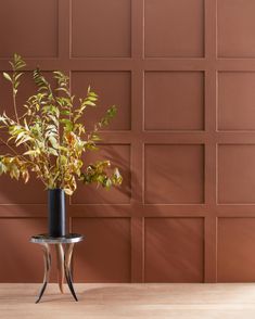 a plant in a vase sitting on a table next to a wall with brown tiles