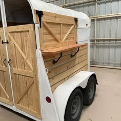 a white horse trailer with wooden doors and windows