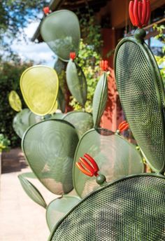 some green and yellow metal sculptures in front of a building with red flowers on them