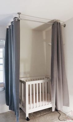 a baby crib in the corner of a room with drapes hanging from it's sides