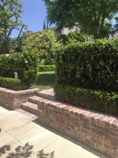 two brick planters sitting on the side of a sidewalk next to trees and bushes