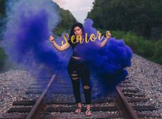 a woman standing on train tracks holding up a sign with the word senior in front of her