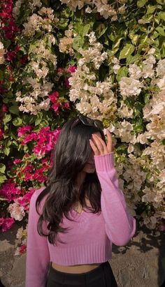 a woman wearing a pink sweater and black skirt standing in front of flowers with her hands on her head