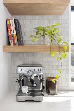 there is a coffee maker on the counter next to books and a potted plant