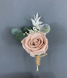 a boutonniere with pink roses and greenery on a gray wall background