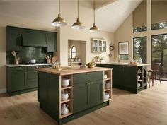 a large kitchen with green cabinets and wooden flooring is pictured in this image, there are three pendant lights hanging from the ceiling