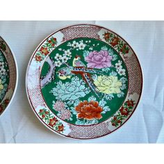 two plates decorated with flowers and birds on white tablecloth, one is green and the other is red