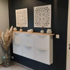 two white vases sitting on top of a counter next to a wall mounted art piece