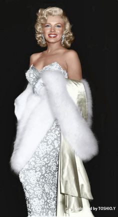 a woman in a white dress and fur stole with her hands on her hips, posing for the camera