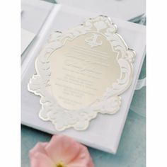 a white and silver wedding card with a flower on it's side, sitting next to some cards