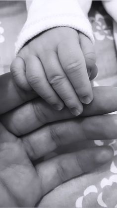 a black and white photo of a baby's hand on top of its mother's finger