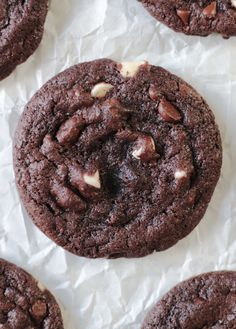 chocolate cookies with white chips on top sitting on wax paper