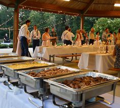 people are standing around tables with food on them and in the background is an outdoor pavilion