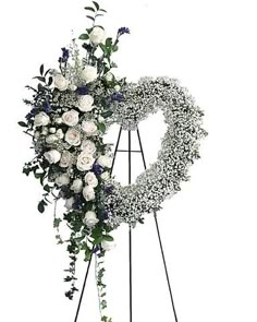 a heart shaped wreath with white flowers and greenery on a tripod easel